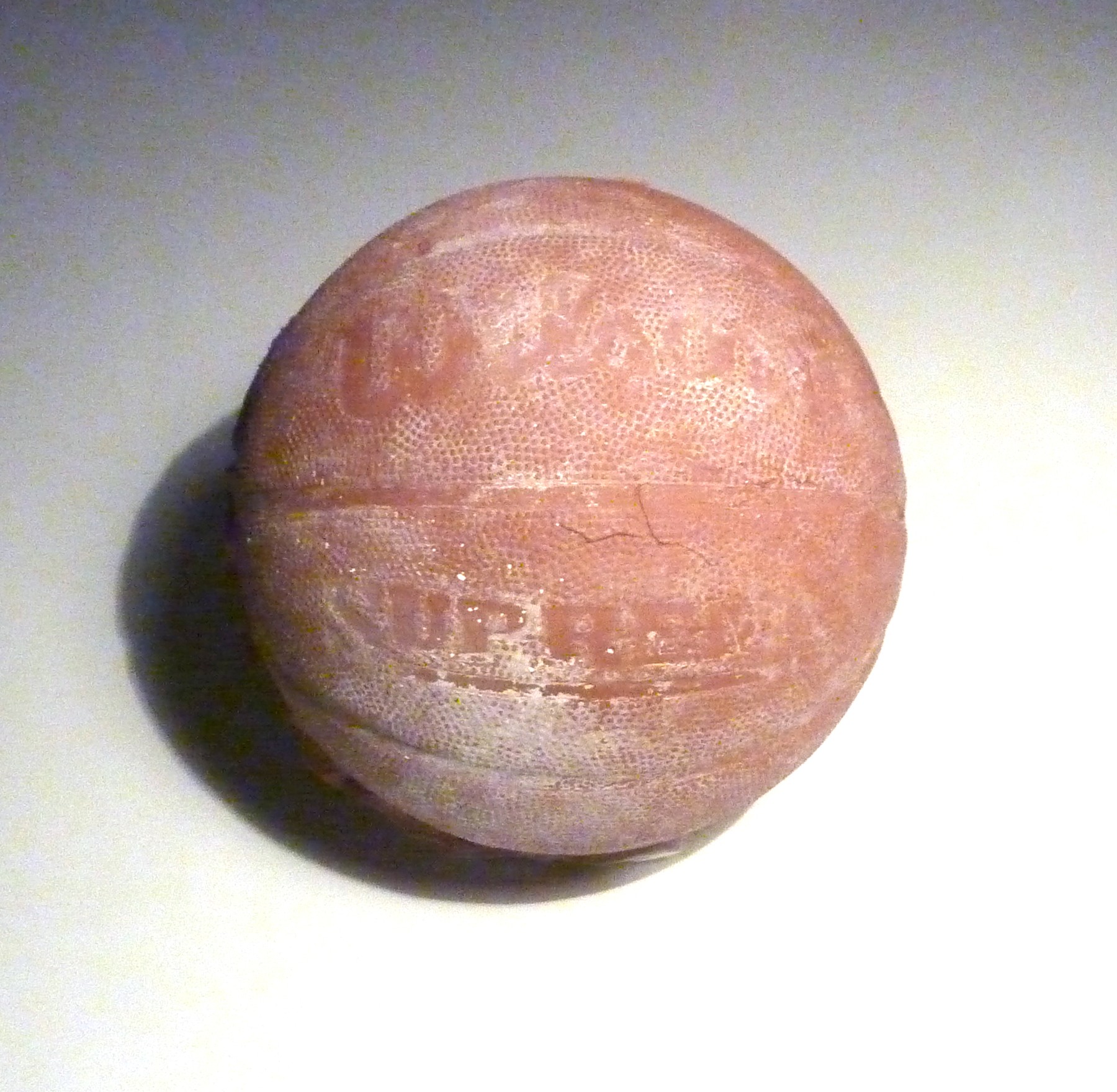Close view of the clay basketball, showing its cast seams and lettering.