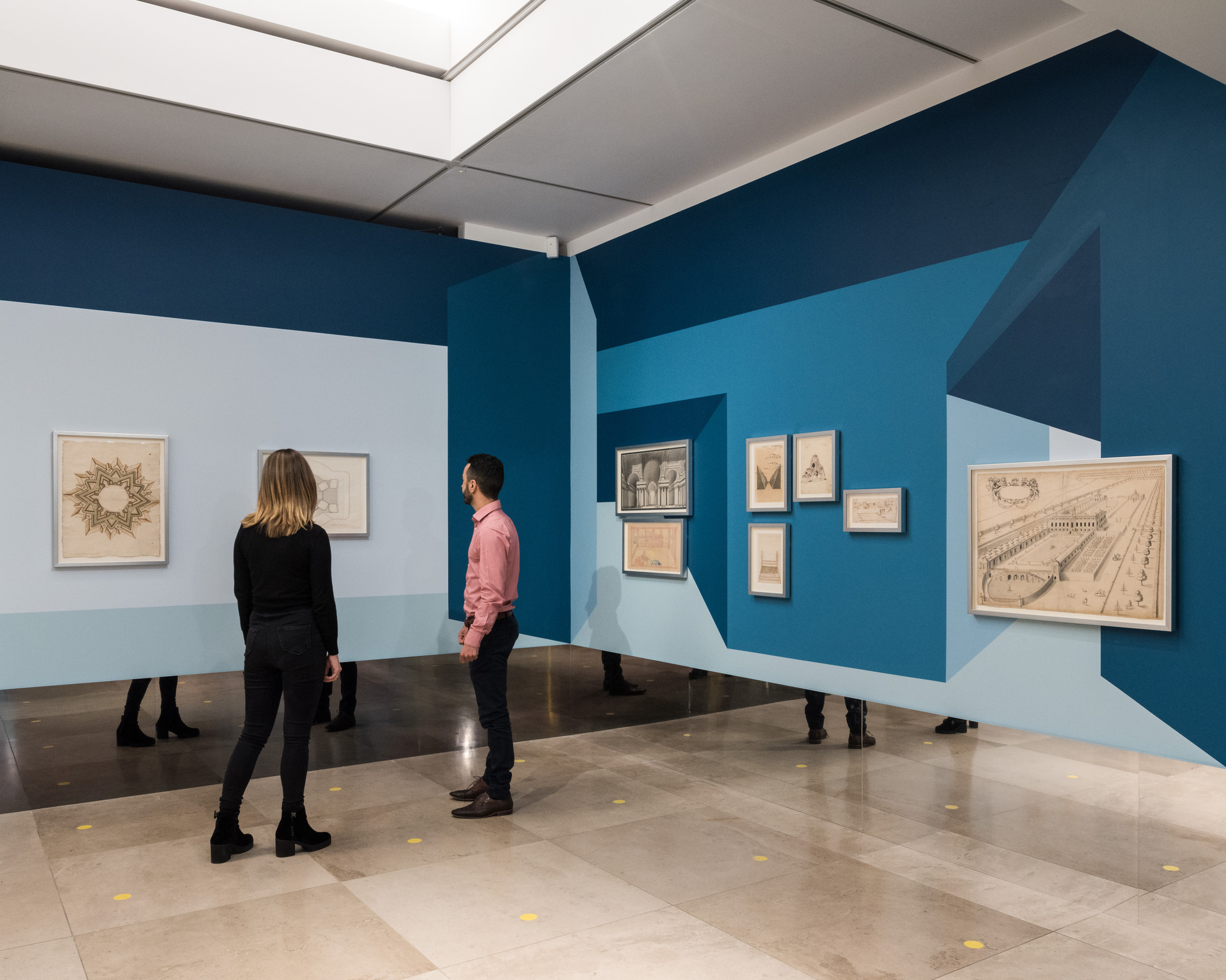 Disappear Here: Visitors looking at drawings with their legs reflected in the mirrored wall base