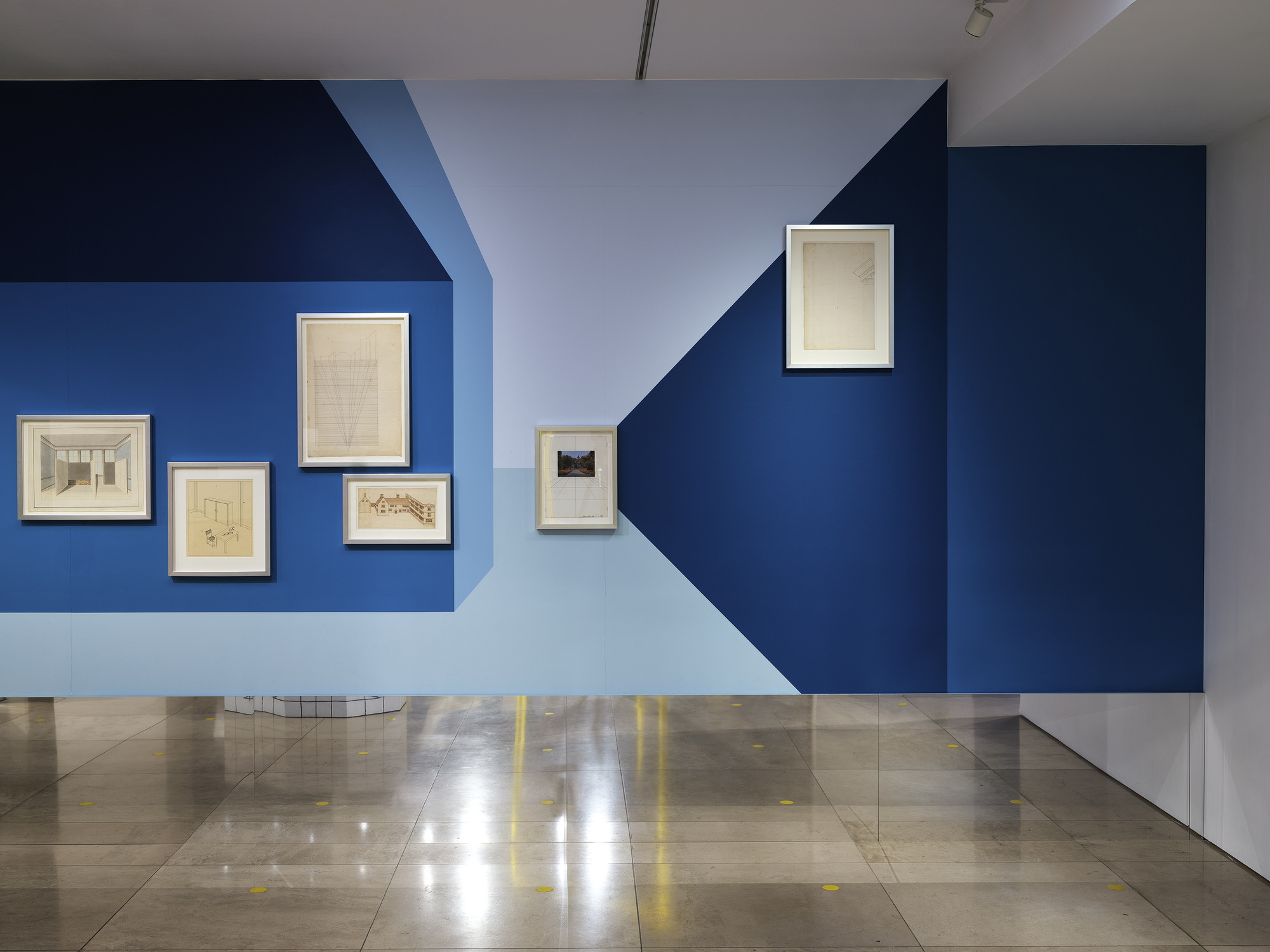 Disappear Here: Drawings hung at different heights on a blue geometric wall painting