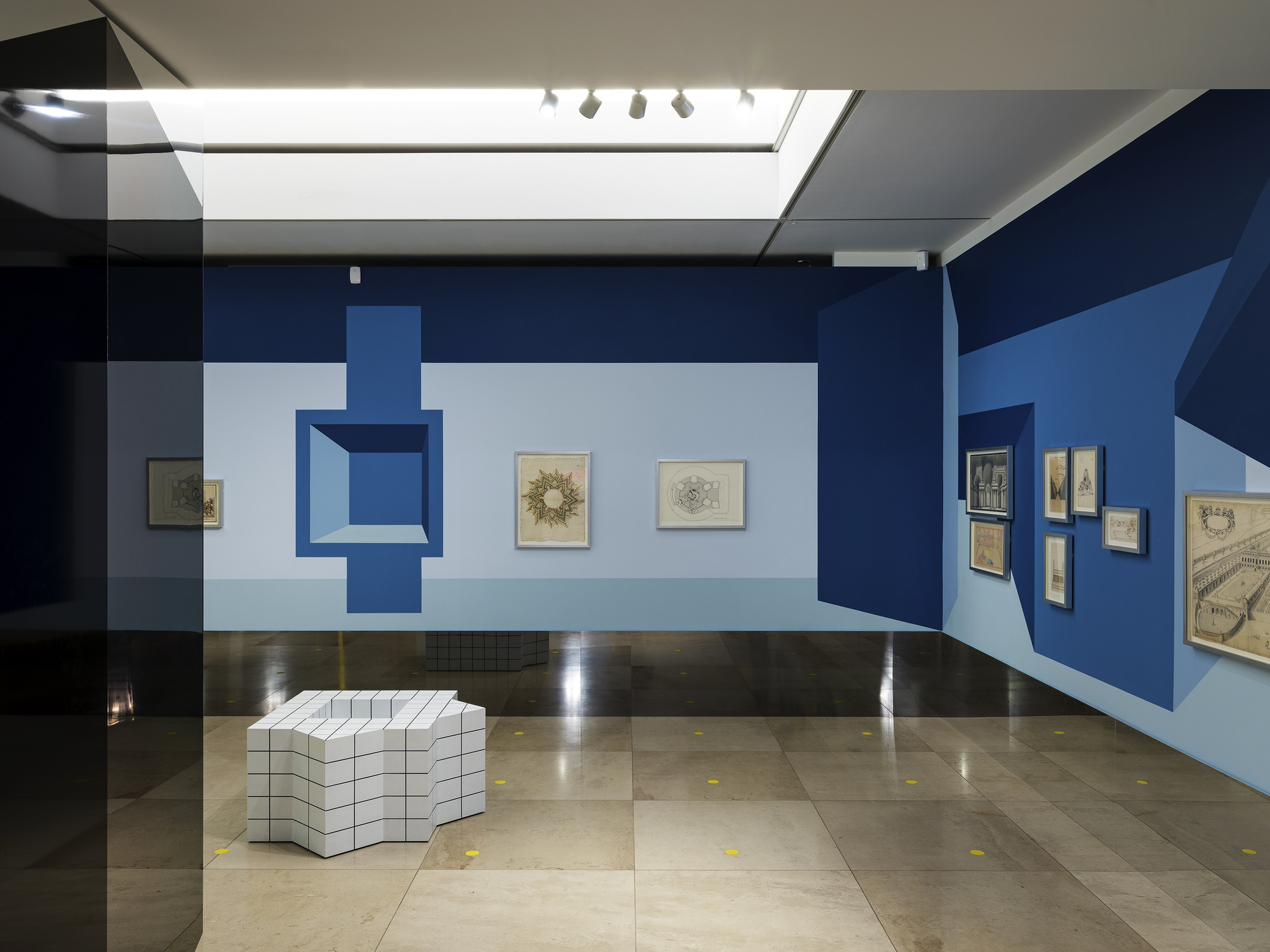 Disappear Here: Exhibition view with blue perspective wall painting, mirrored column and gridded seat